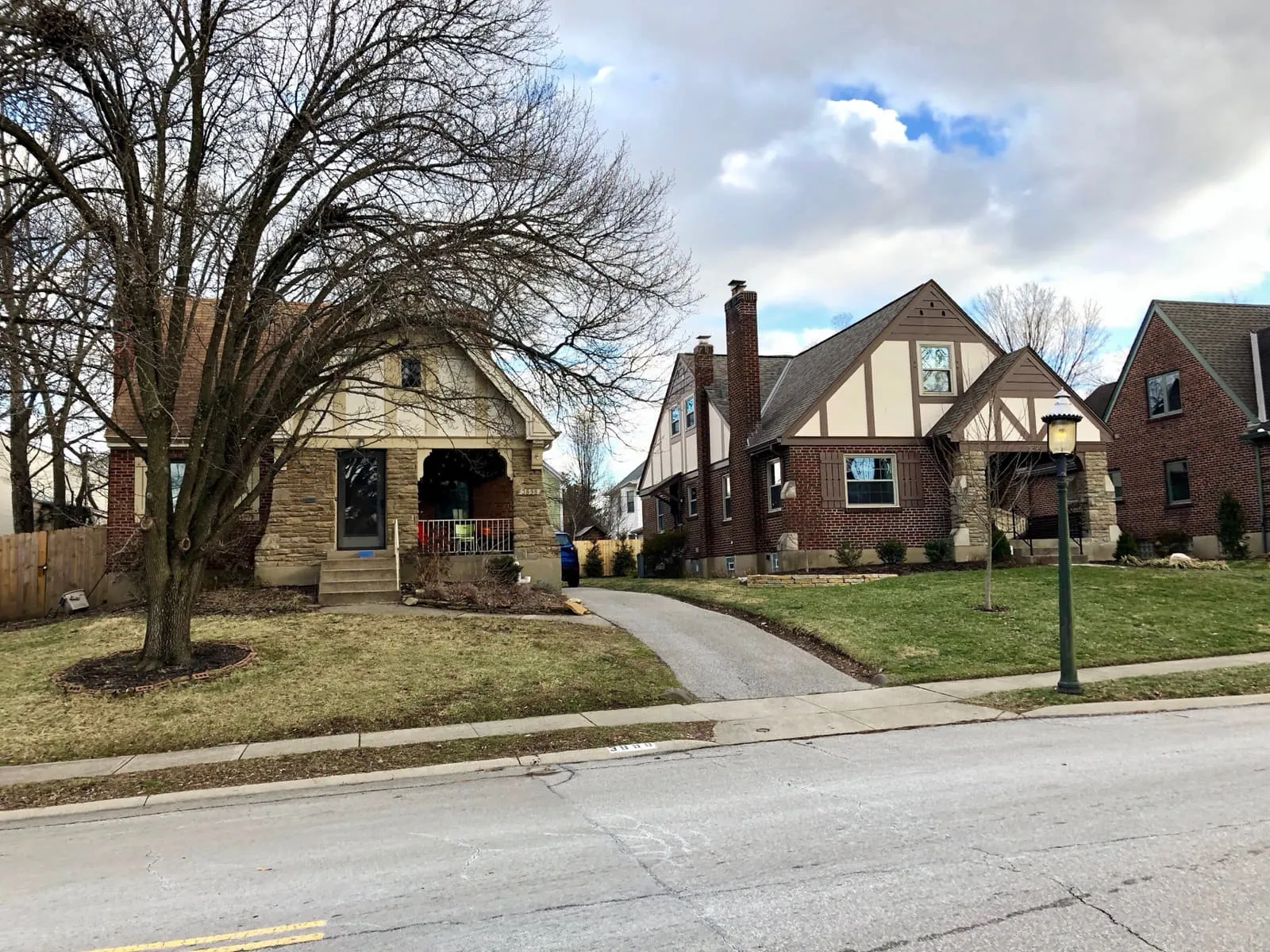 A stone-fronted bungalow and a Tudor Revival house with a brick chimney, on a residential street in Oakley, Cincinnati, on a winter afternoon.
