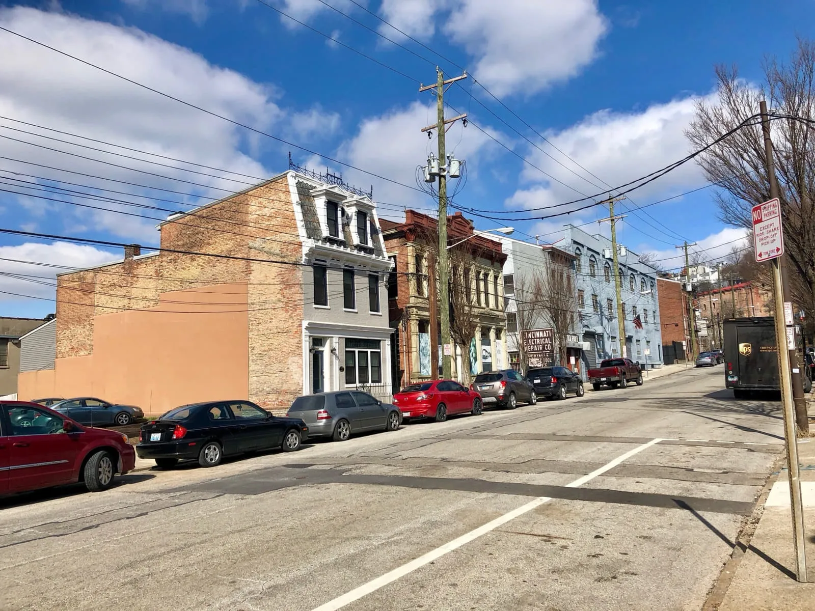 A block of nineteenth-century brick buildings on Elm Street in Over-the-Rhine, Cincinnati, under overhead power lines, with a painted sign reading Cincinnati Electrical Repair Co.